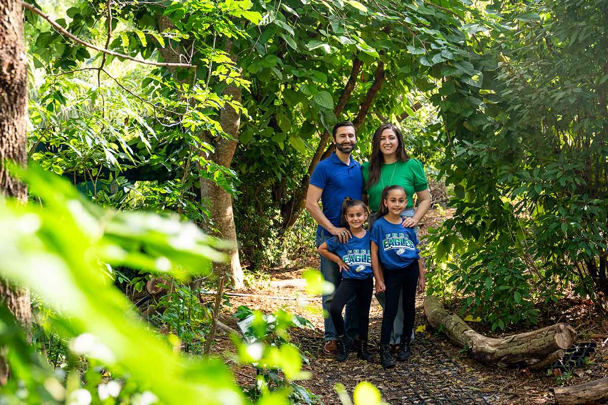 Two adults and two children dressed in FGCU green and blue stand in the FGCU Food Forest