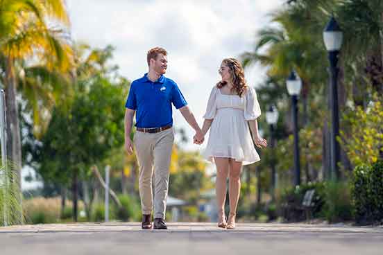 A man in a blue shirt and a woman in a short white dress holding hands and walking outdoors