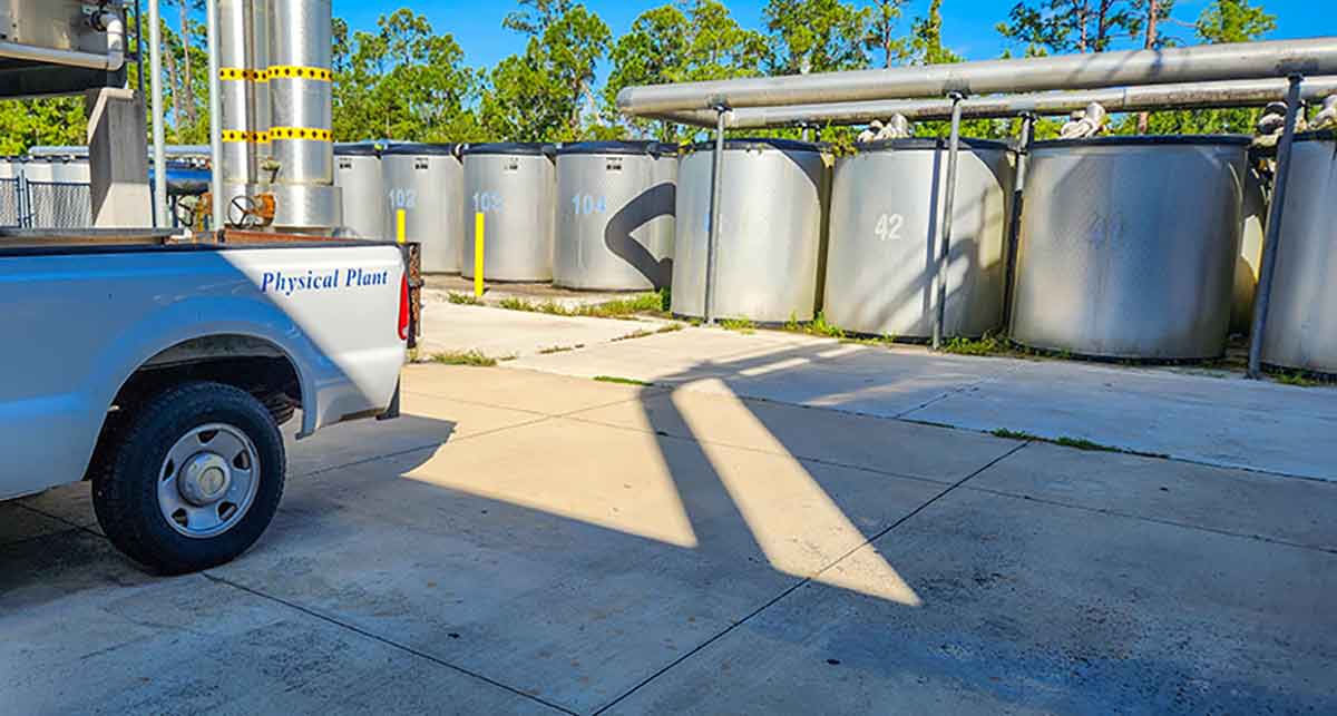 A white pickup truck with the words physical plant on the side is parked near numbered ice storage tanks