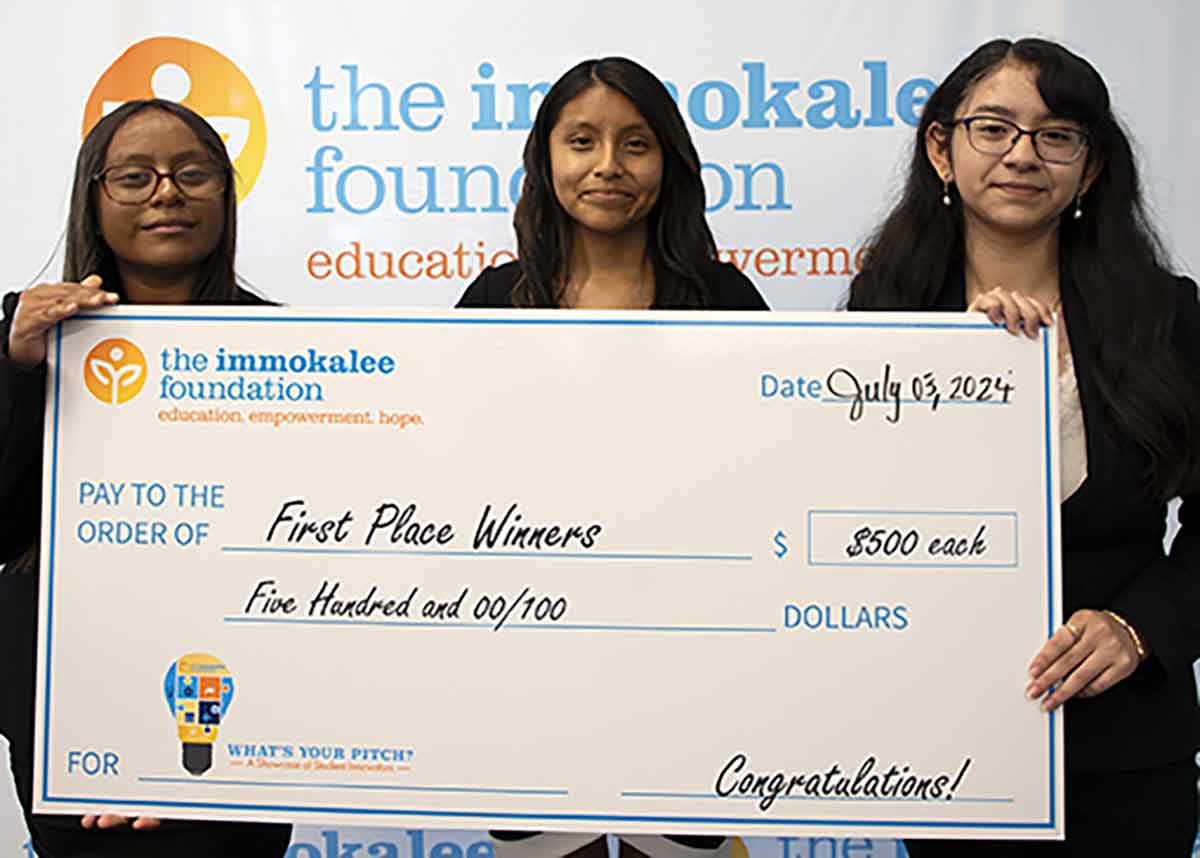 Three young women hold a giant check that reads First Place Winners