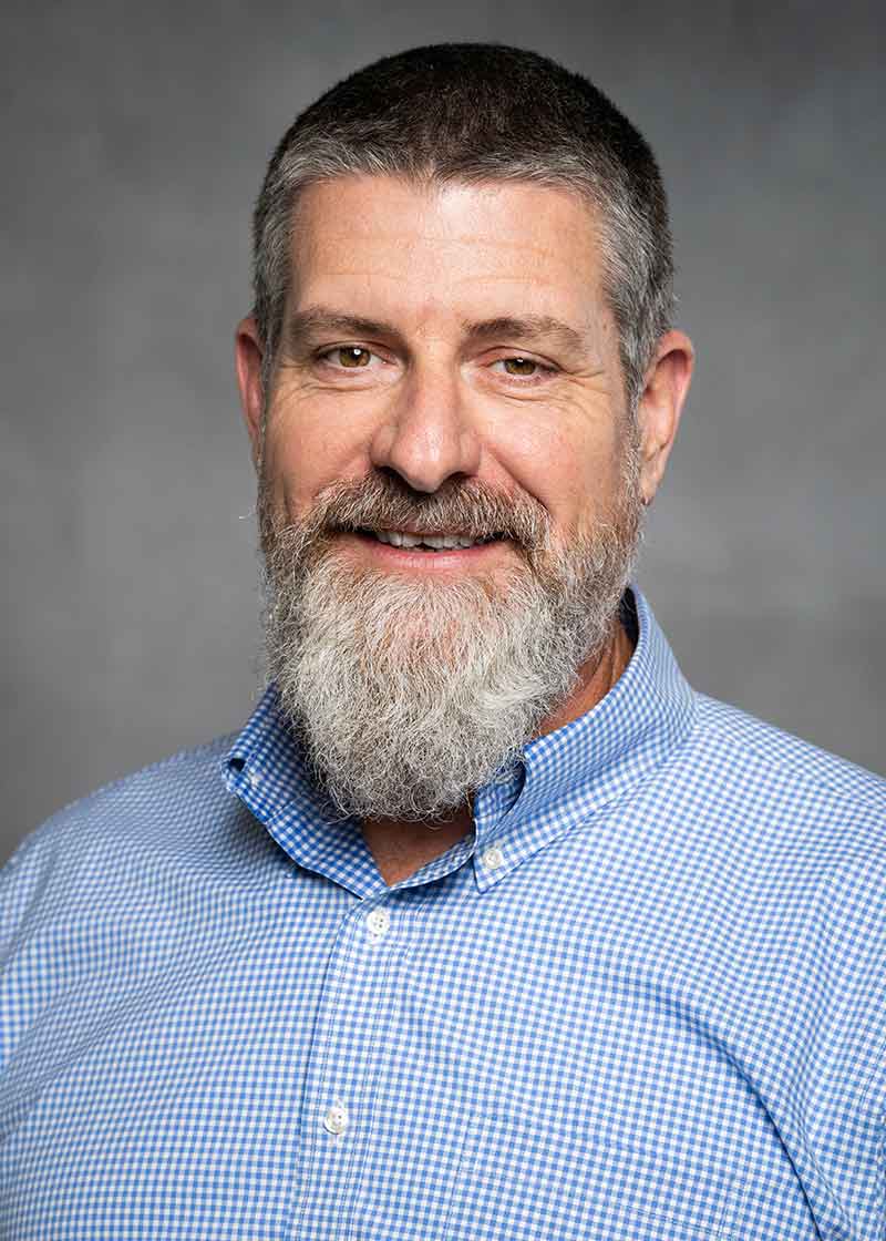 A smiling man with a beard and mustache and blue button-down shirt