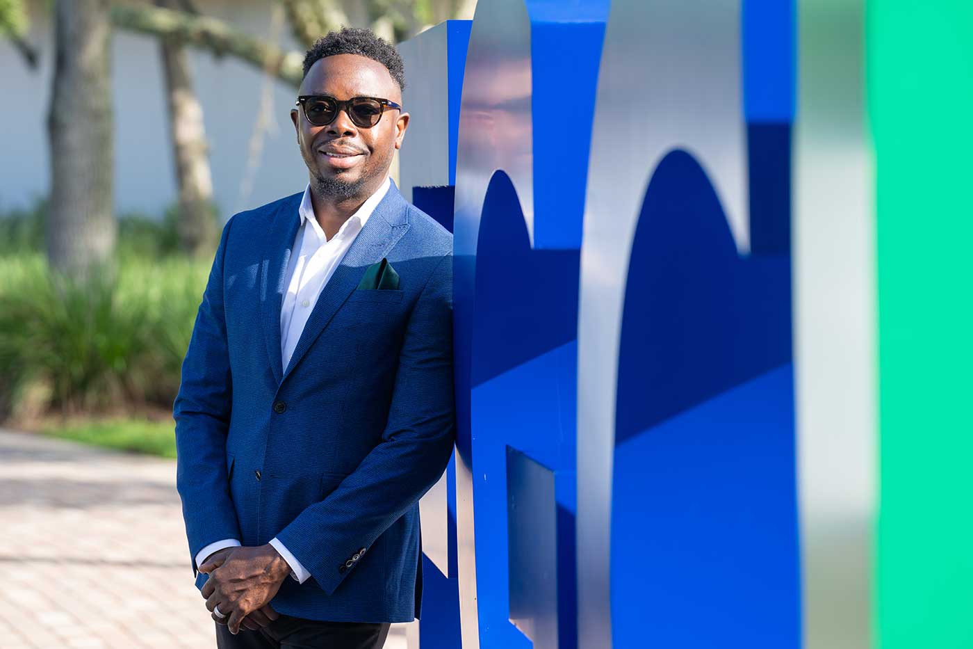 FGCU graduate Judes Sétalaire Albert standing in front of the FGCU logo on the Library Lawn on campus.