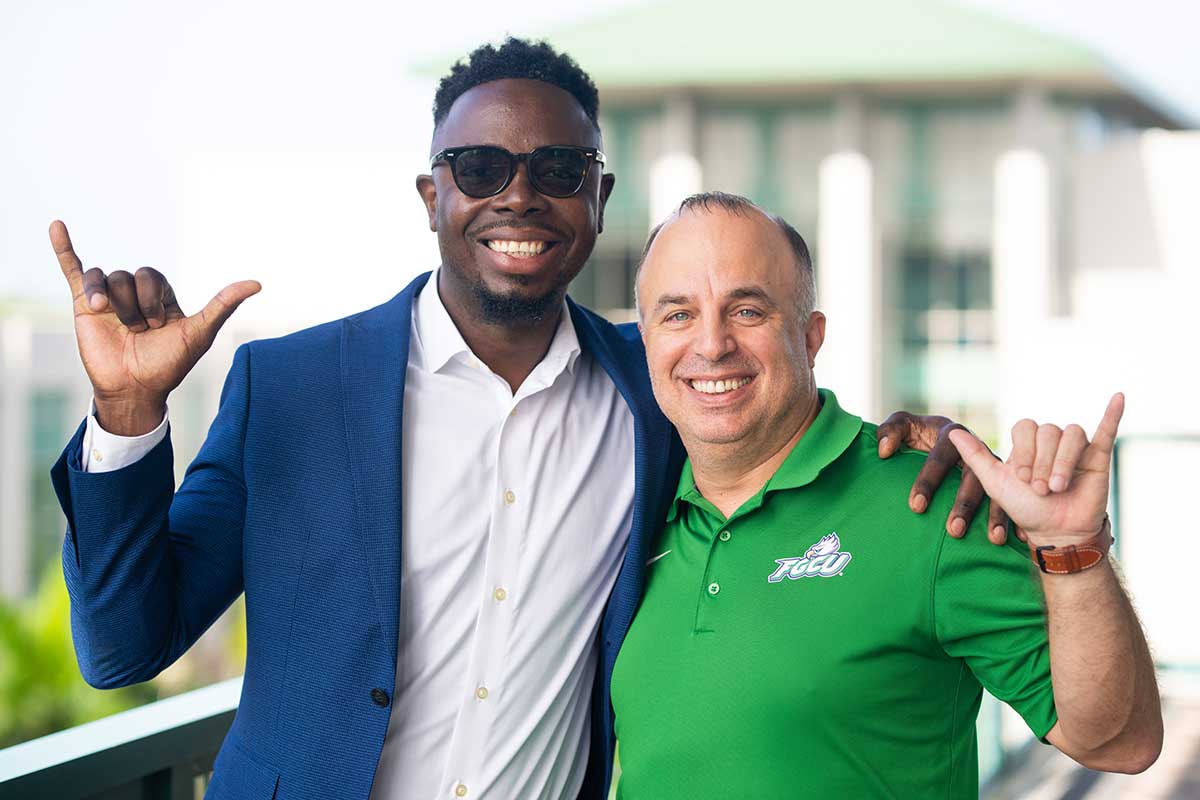 FGCU graduate Judes Sétalaire Albert standing next to his mentor, FGCU professor Tom Felke, on the FGCU campus doing the Wings Up gesture.