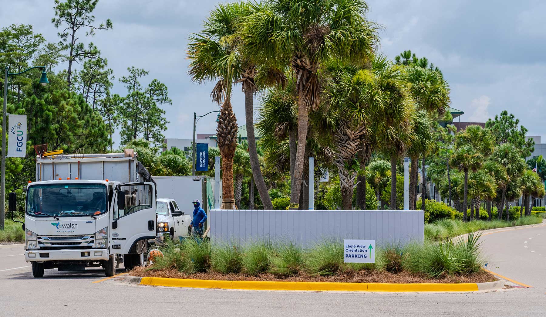 Photo shows landscaping and workers installing new digital signage at the main entrance to Florida Gulf Coast University.