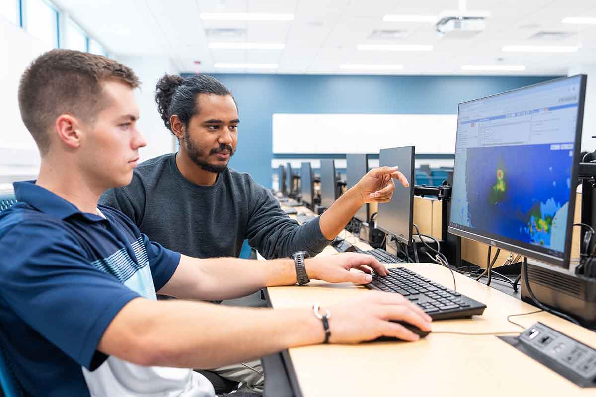 Two young men sit in front of a computer