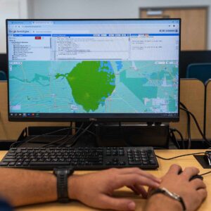 A computer screen with an image from NASA Earth Observations program. Two hands are seen on a desk controlling a computer mouse.