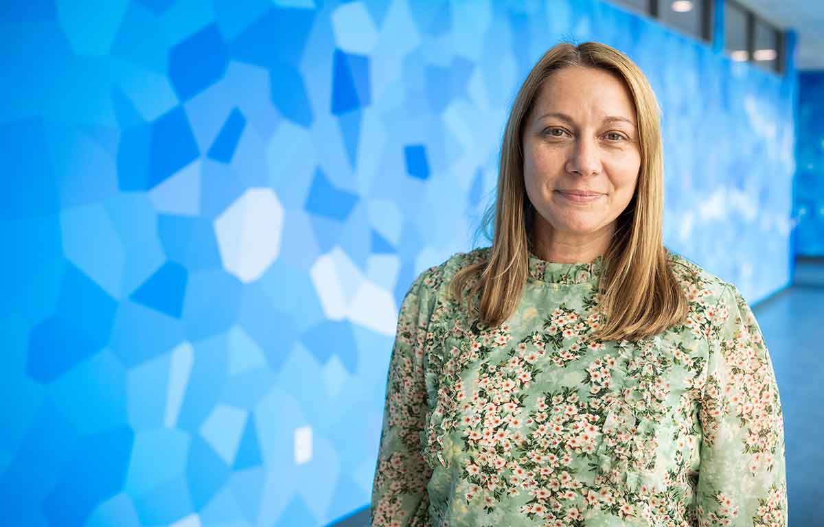 A woman in a green and white shirt stands in front of a blue wall