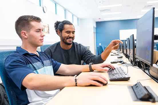 Two young men sit in front of a computer