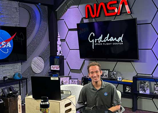 FGCU grad Brandon Cominsky sits in a chair in the communications studio at Goddard Space Flight Center.