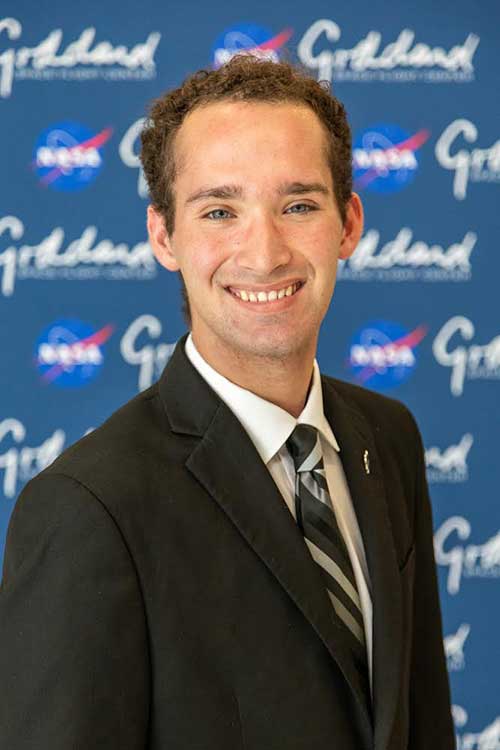 FGCU grad Brandon Cominsky stands in front of a sign reading Goddard Space Flight Center.