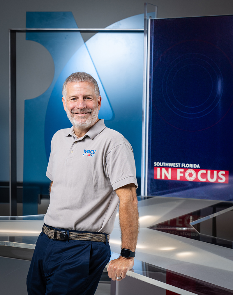 Man in gray shirt standing on the set of news show in studio