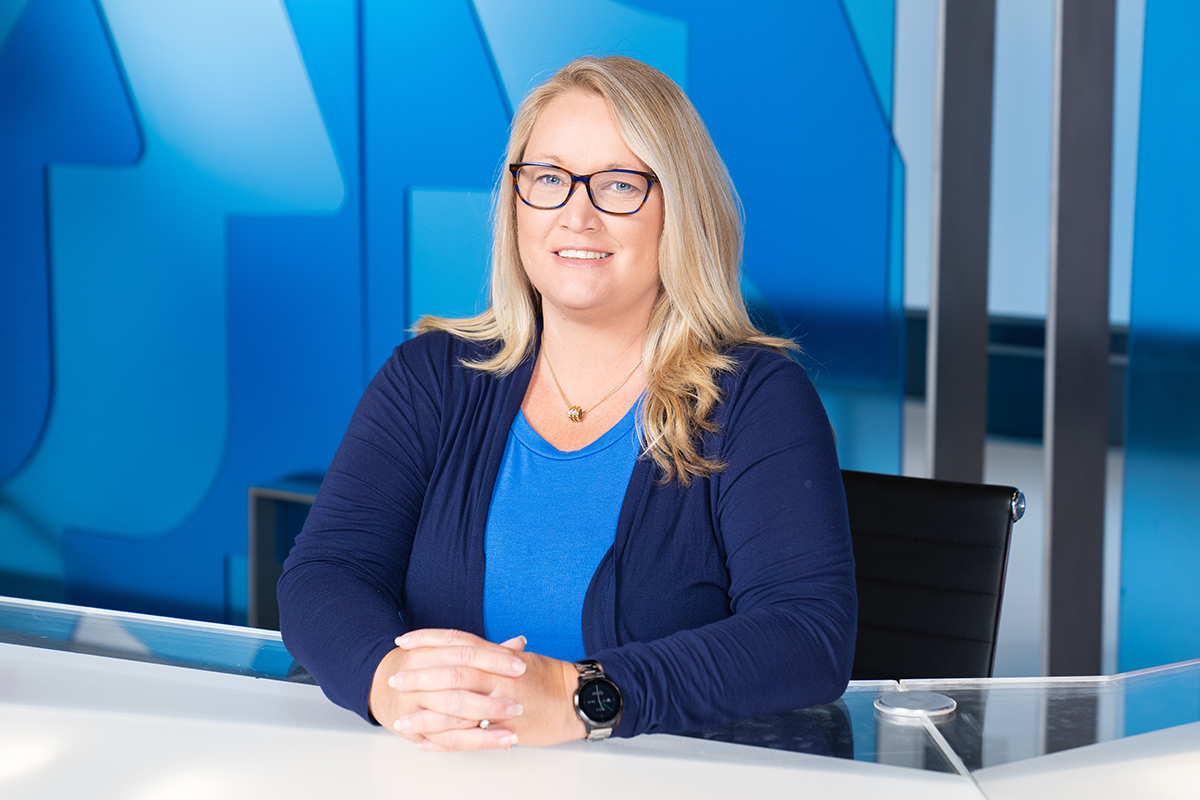 Woman in blue shirt and sweater sitting at desk in TV studio