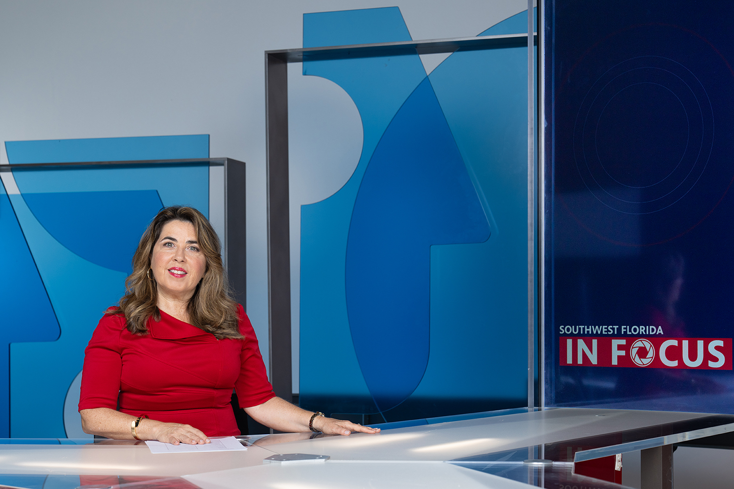 Woman in red dress sitting a desk on set in TV studio