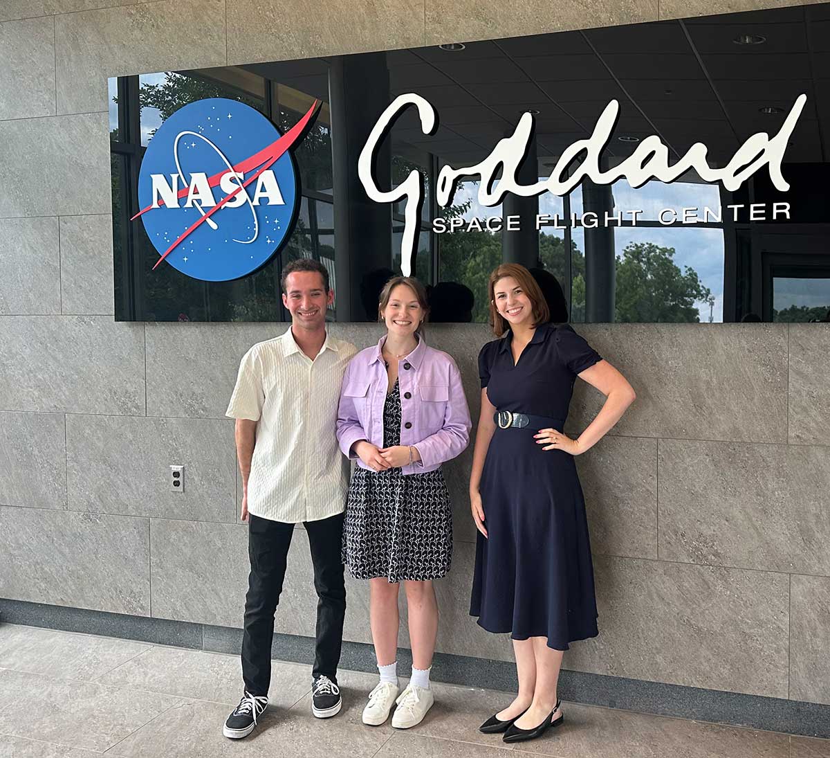 FGCU grad Brandon Cominsky stands in front of a sign reading Goddard Space Flight Center with two other people.