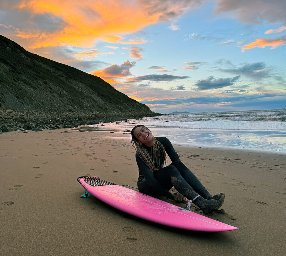 Woman sitting in sand next to surfboard at beach