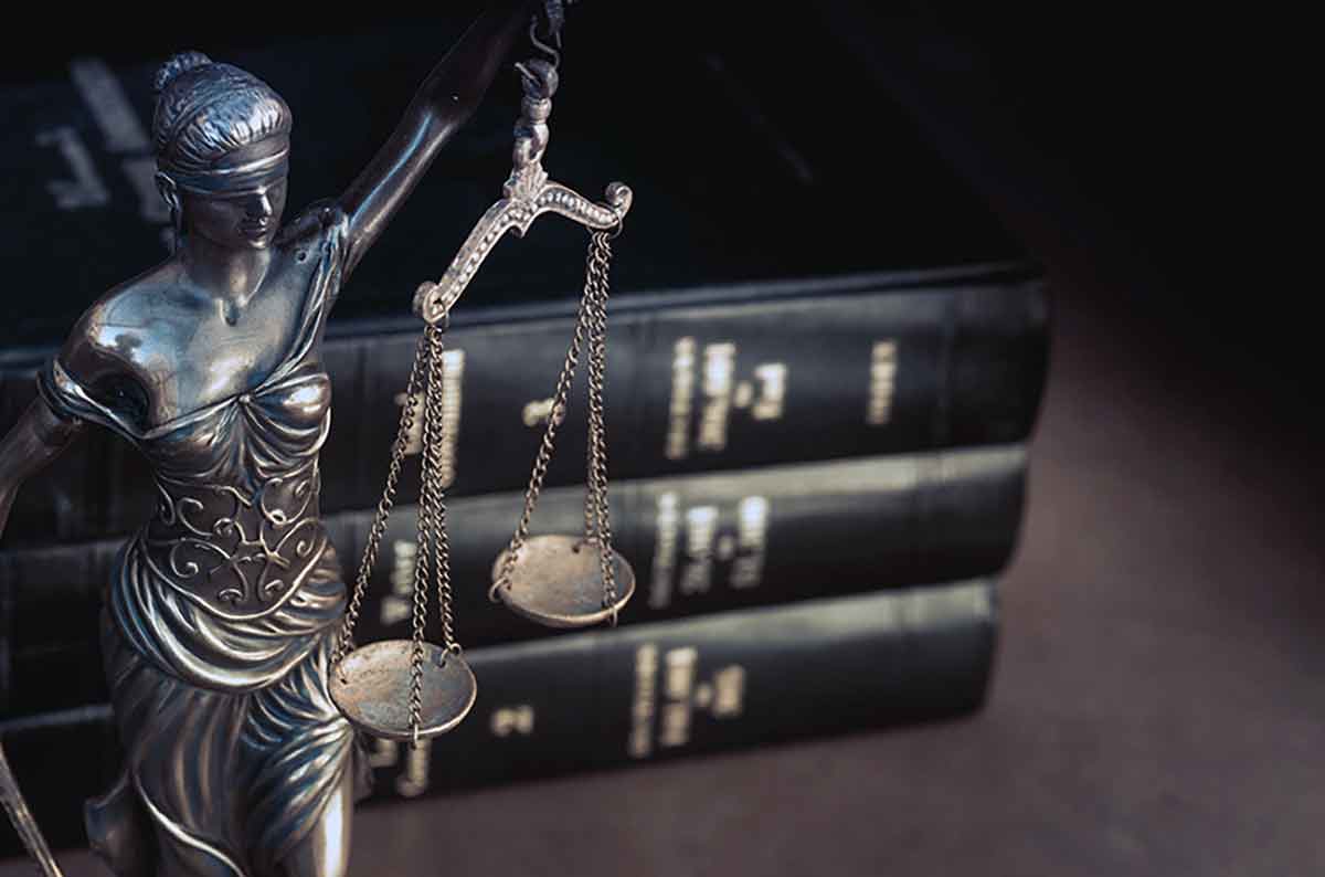 A statue of a blindfolded woman holding scales, in front of three hardcover books