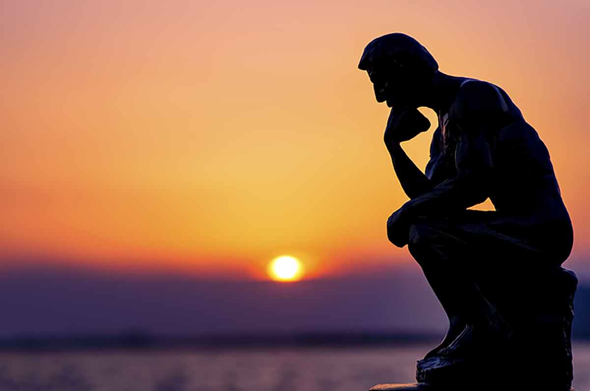 The thinking man statue in silhouette with a setting sun in the background