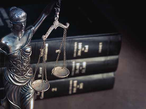 A statue of a blindfolded woman holding scales, in front of three hardcover books