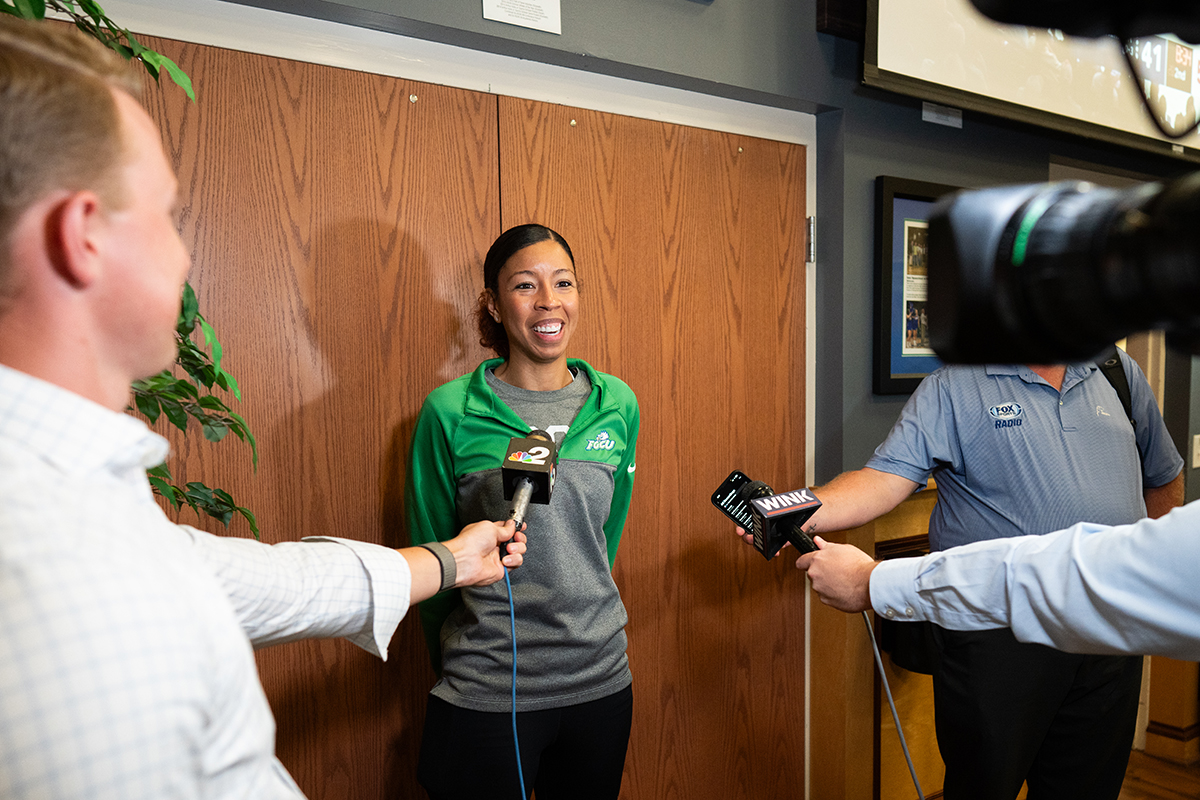 Woman in track jacket being interviewed by TV news crews