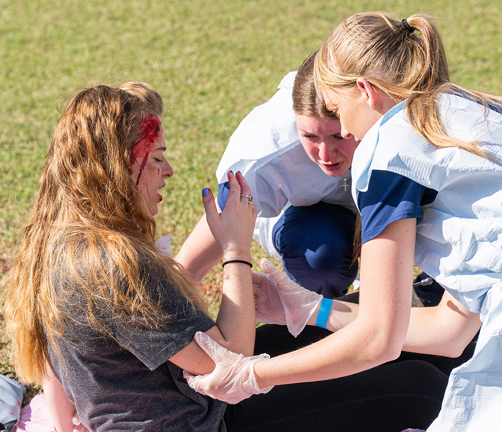 A woman wearing fake blood is tended to by two women students in a simulated disaster drill.