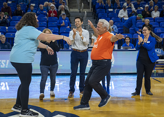 man running with open arms toward woman on basketball court