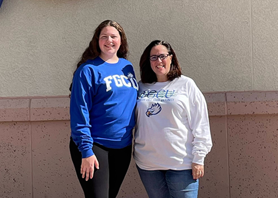 A young woman in a blue FGCU sweatshirt and her mom, wearing a white FGCU long-sleeve shirt, pose for the camera