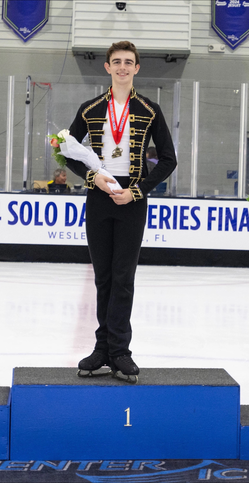 Man in ice skating costume standing on podium and holding flowers