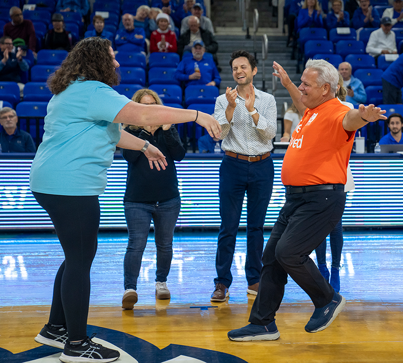 man running with open arms toward woman on basketball court