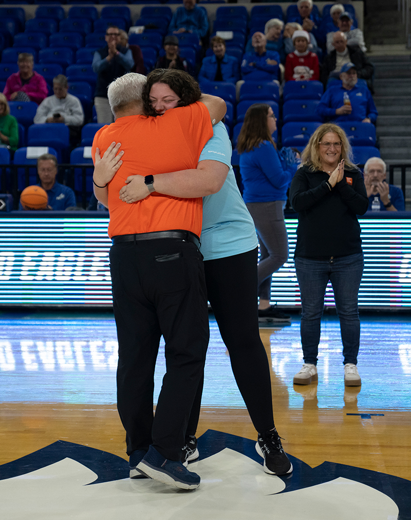 man running with open arms toward woman on basketball court