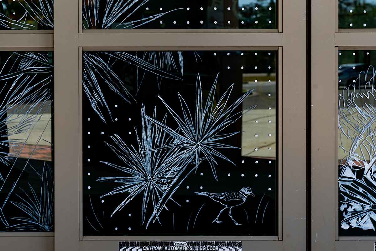 A close-up of the design on a window is of a line drawing of saw palmetto and a bird surrounded by a grid of white dots