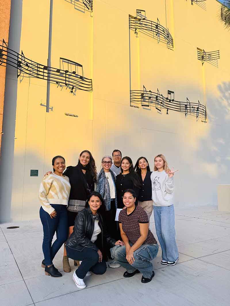 A group of students stand in front of a beige building with large, metal musical notes and a score affixed to the side.