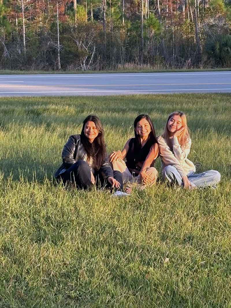 Three female students sit in the grass