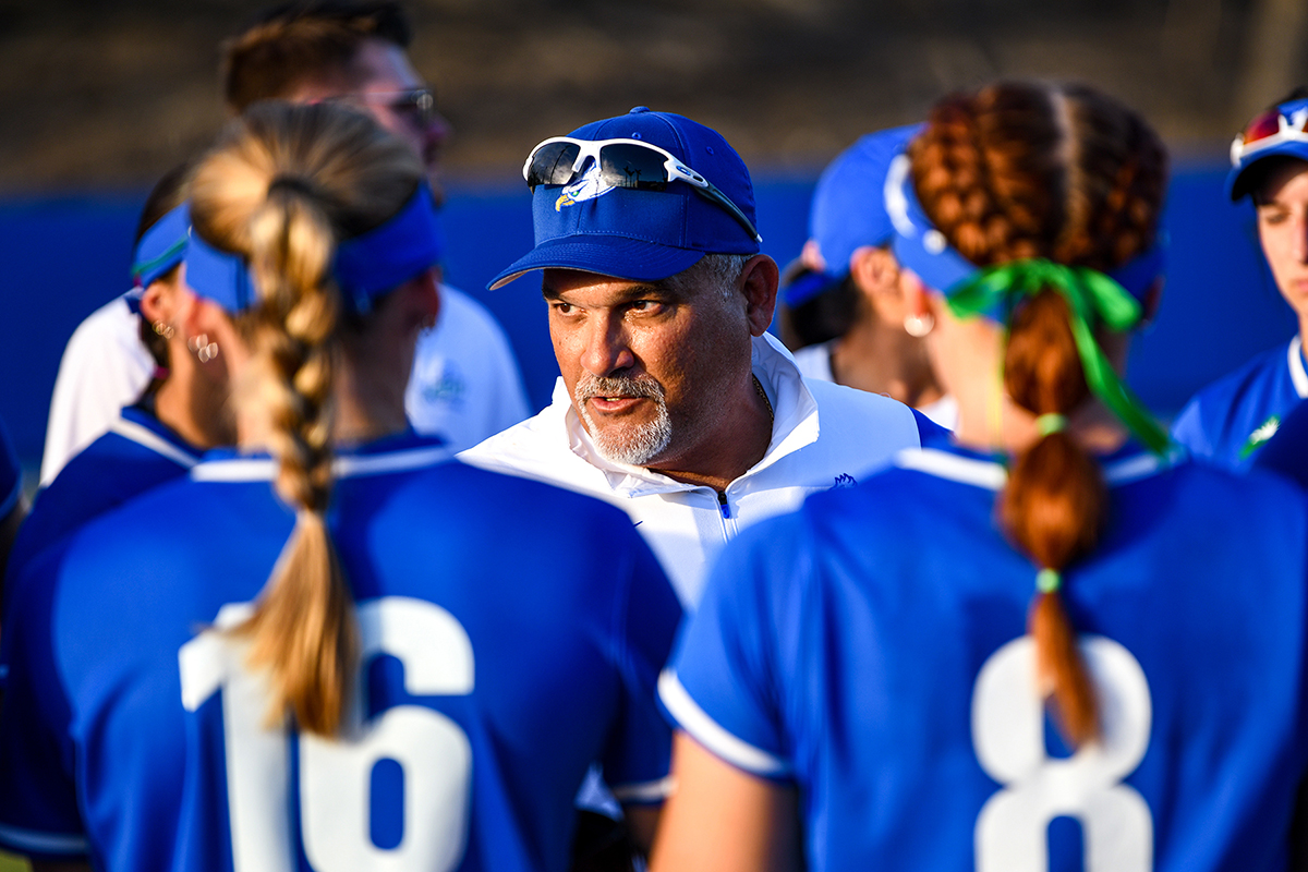 man in white shirt and blue hat and cap talking to athletes in uniform