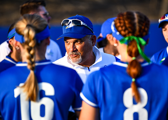 man in white shirt and blue hat and cap talking to athletes in uniform