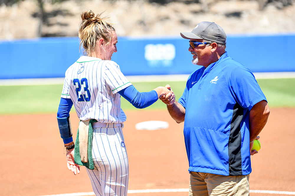 female softball player in uniform shaking hands with make coach in blue shirt