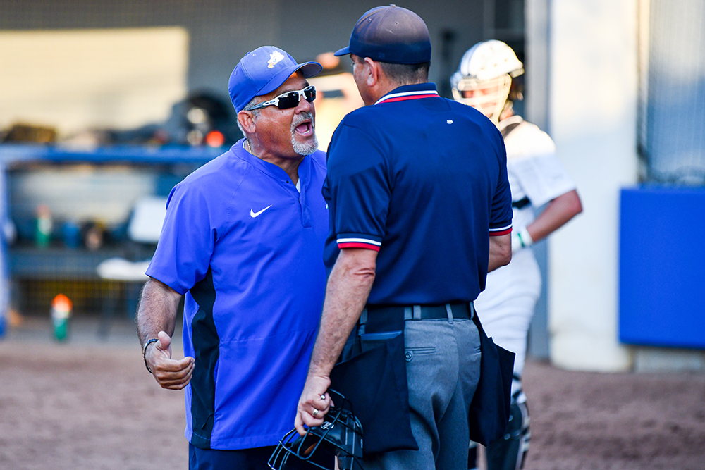 man in blue shirt arguing with softball umpire