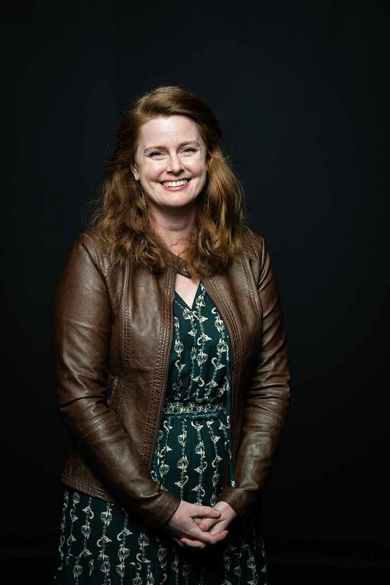 A woman in a green dress and brown leather jacket