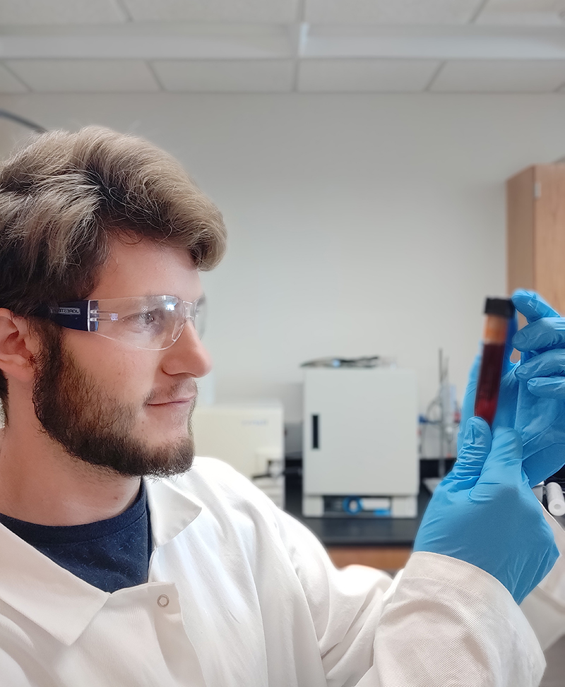 Man in white lab coat looking at specimen in vial