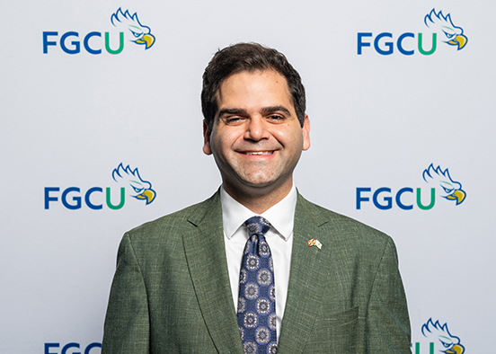 Man in dark gray suit and blue tie smiling for photo