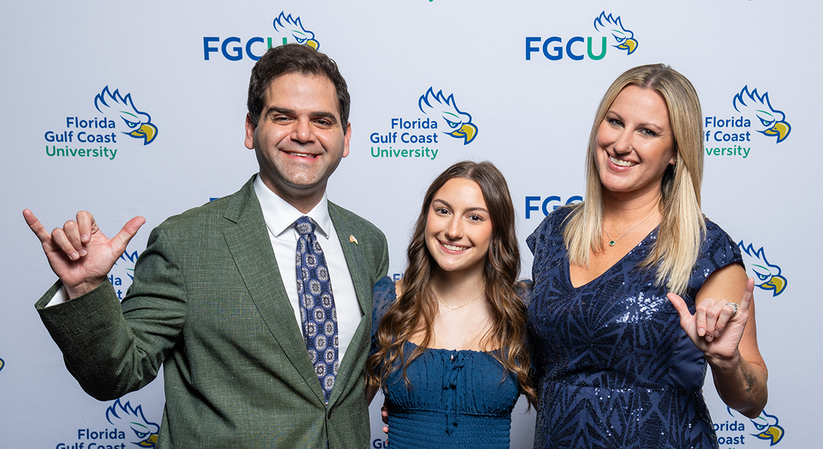 Man in gray jacket and blue tie standing next to girl in blue dress and woman in blue dress