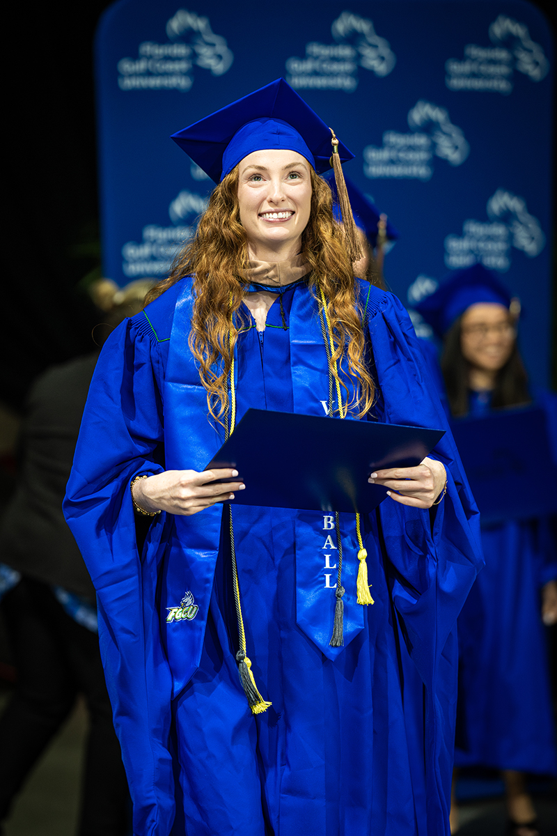 Woman in cape and gown holding her diploma at commencement