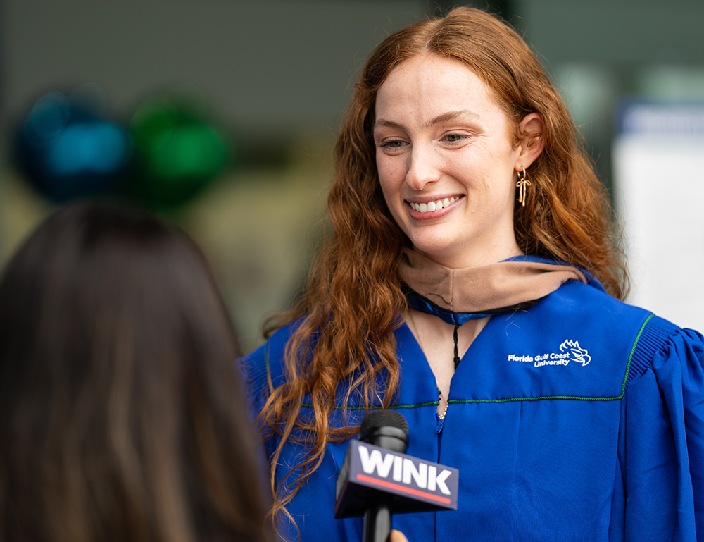 woman in commencement gown being interviewed by TV reporter