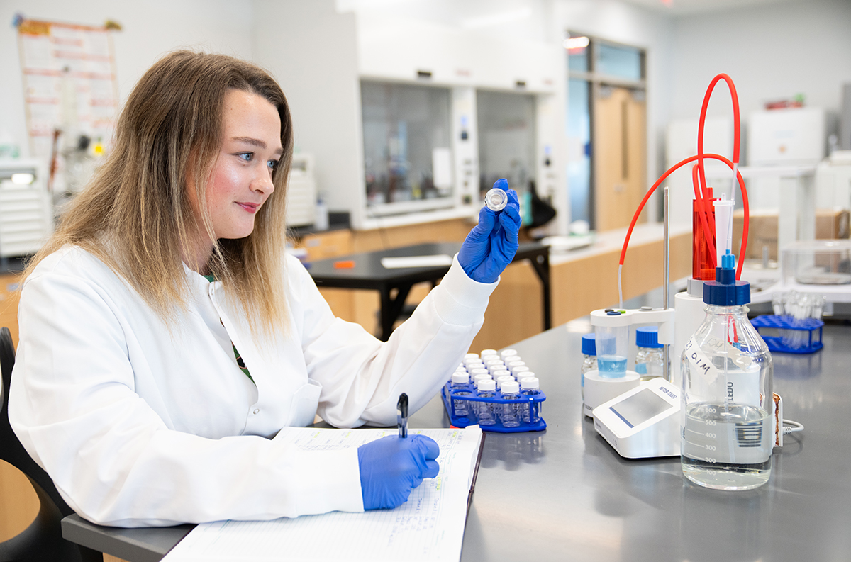 Woman in white lab coat looking at vial in laboratory