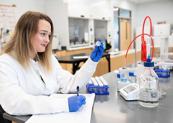 Woman in white lab coat looking at vial in laboratory