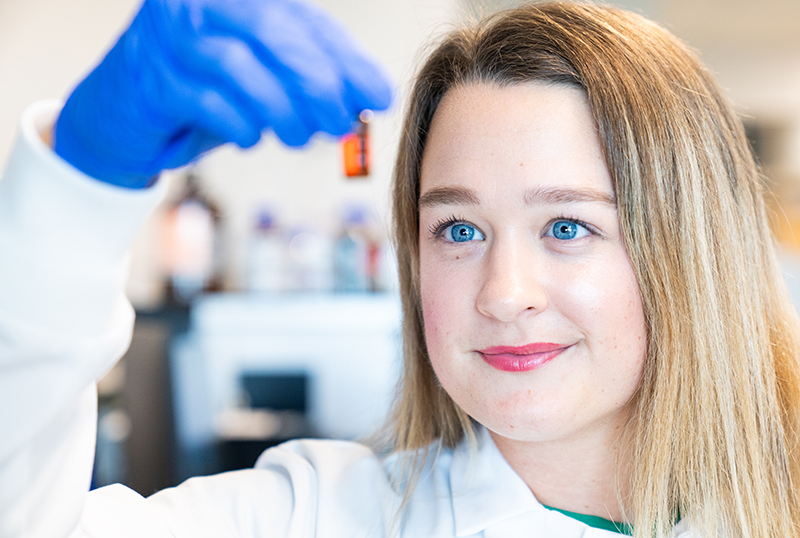 Woman in white lab coat looking at vial in laboratory