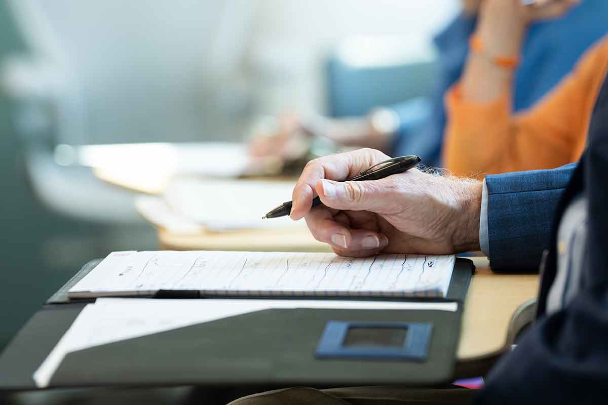 Image of three disembodied hands holding pens and taking notes; only the first hand is in focus