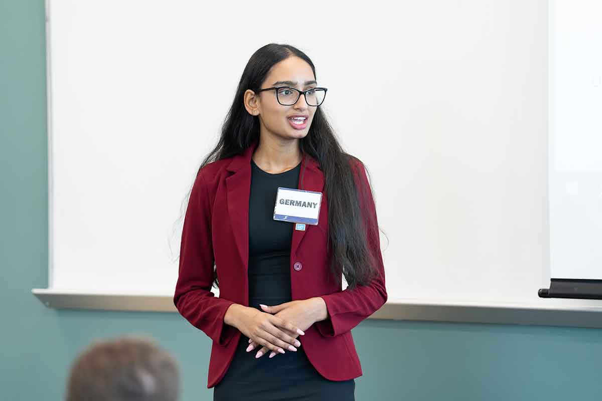 A young woman in a burgundy blazer wearing glasses with a nametag that says Germany