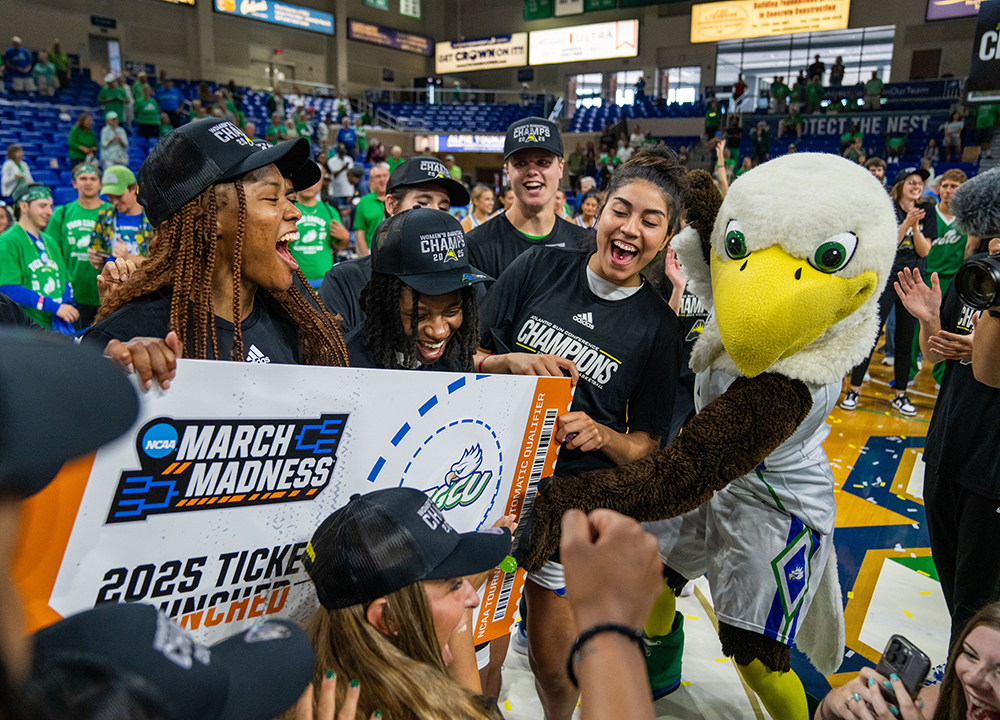 Women basketball players celebrate with FGCU mascot