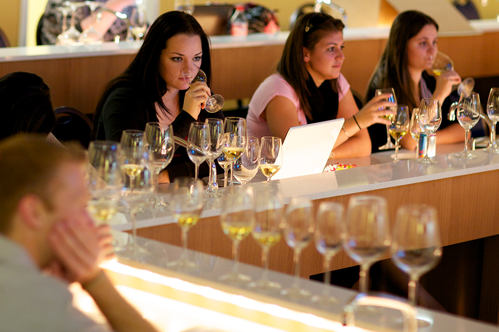 Three female students tasting wine in a classroom