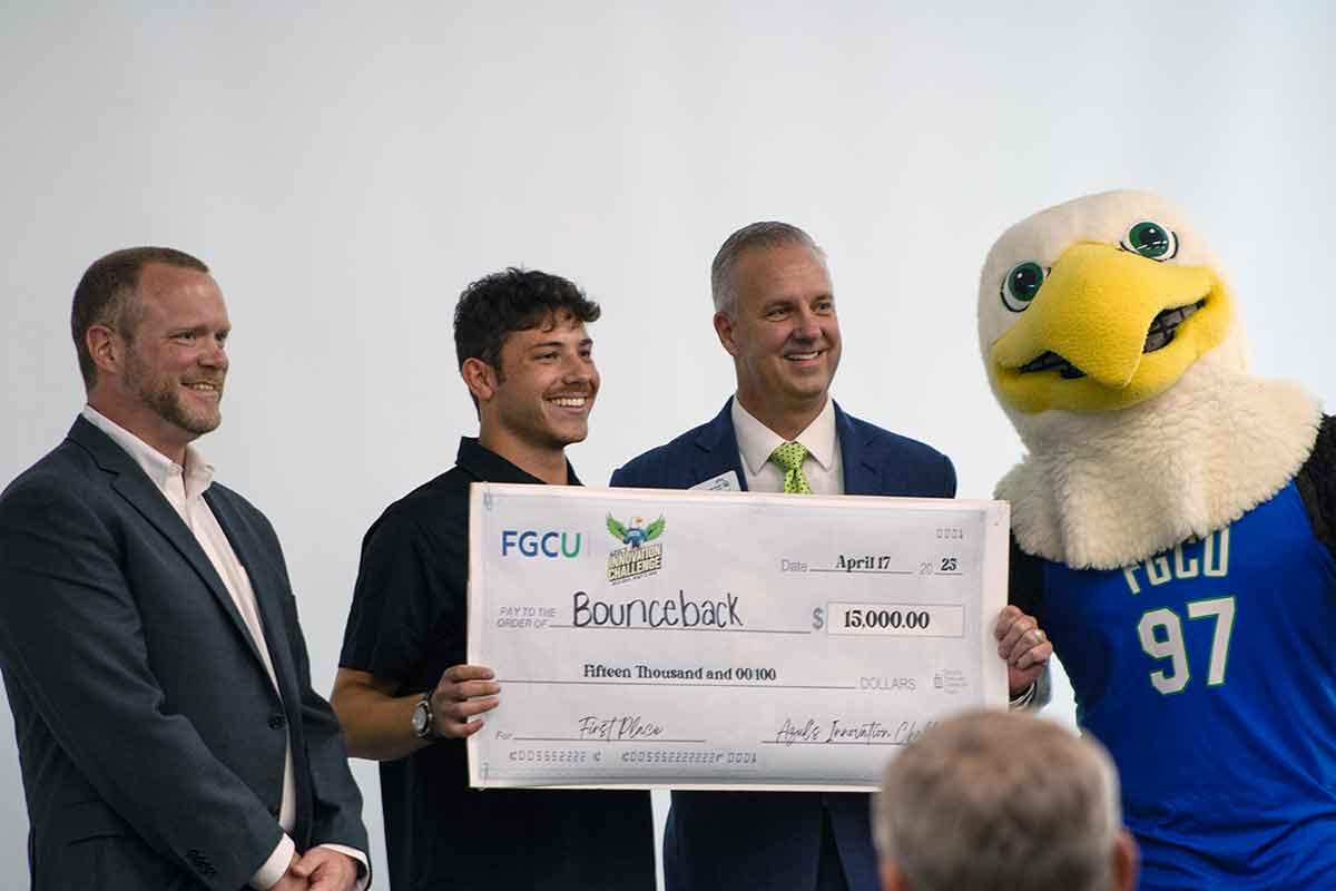 Three men and Azul, the FGCU eagle mascot, stand, smiling and holding an oversized check for fifteen thousand dollars
